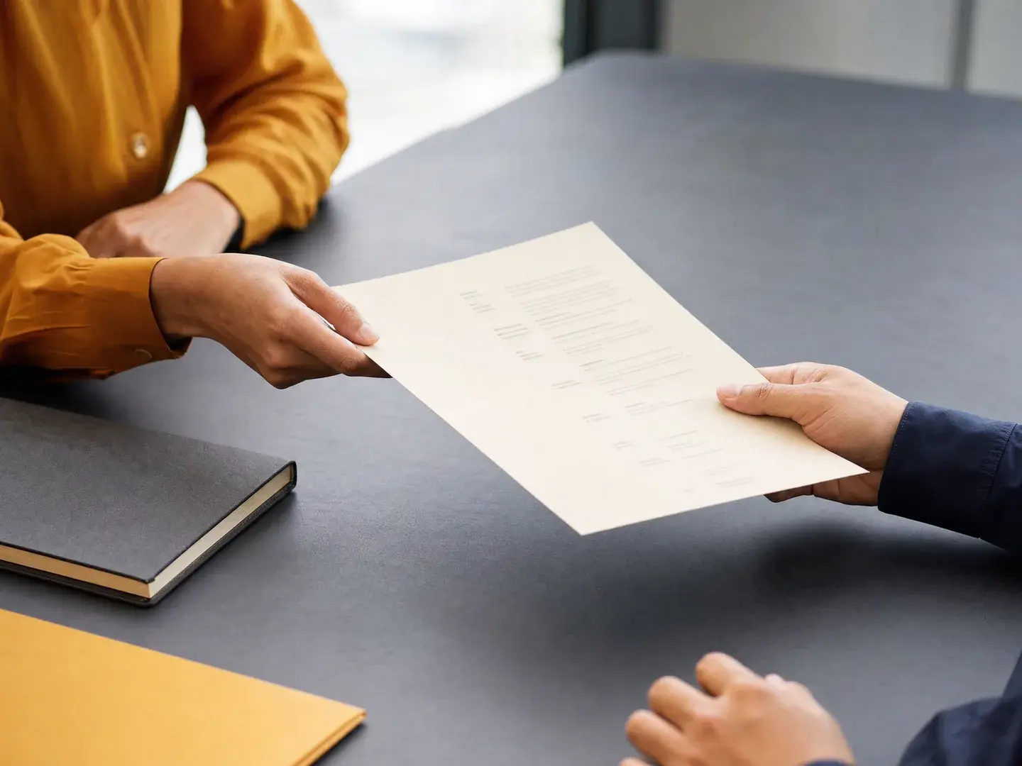 Twee paar handen die een projectbrief overdragen aan een vergadertafel