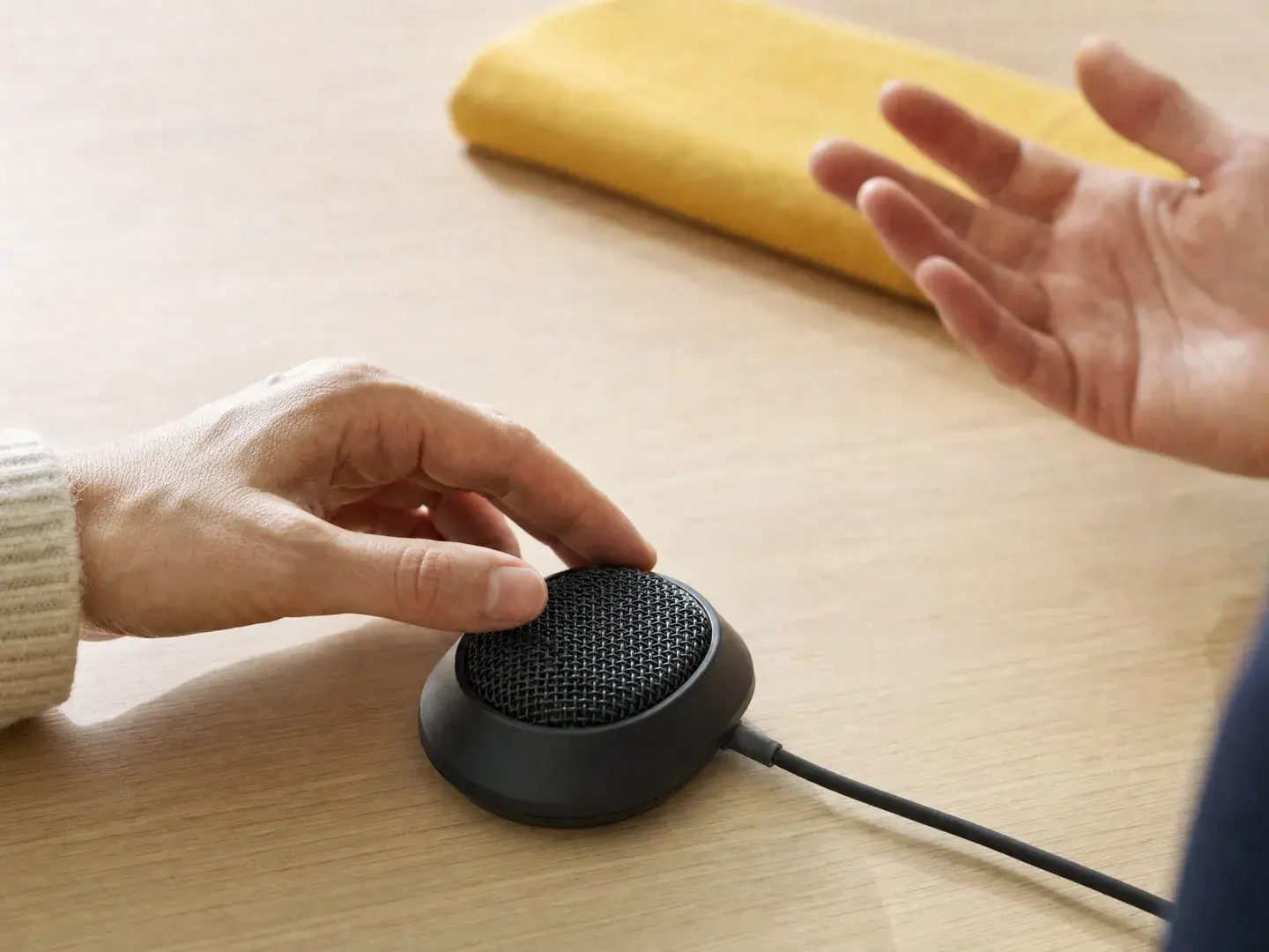 Handen bespreken een vraag via een compacte vergaderluidspreker op een lichte tafel