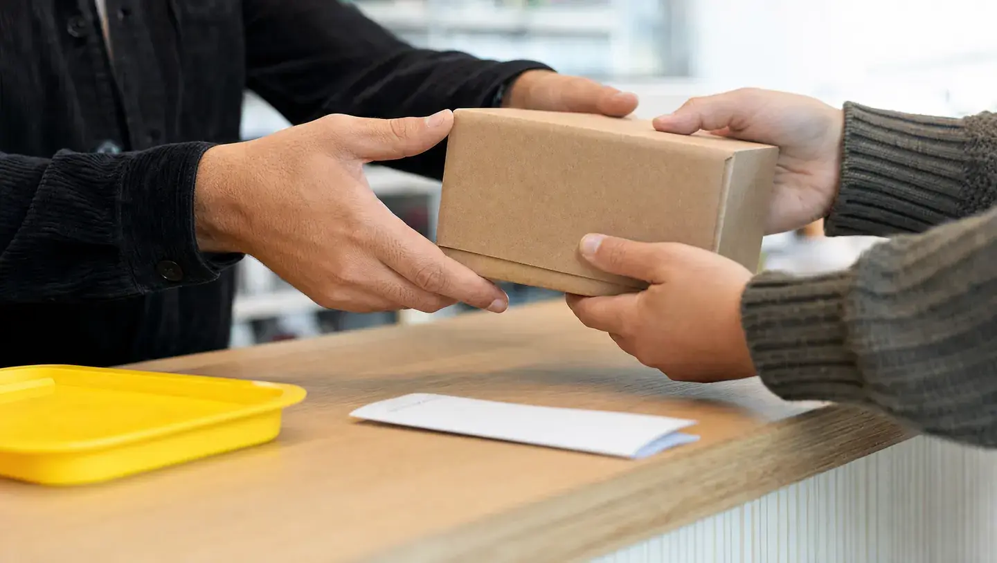 Twee paar handen geven een kartonnen pakket over een houten balie